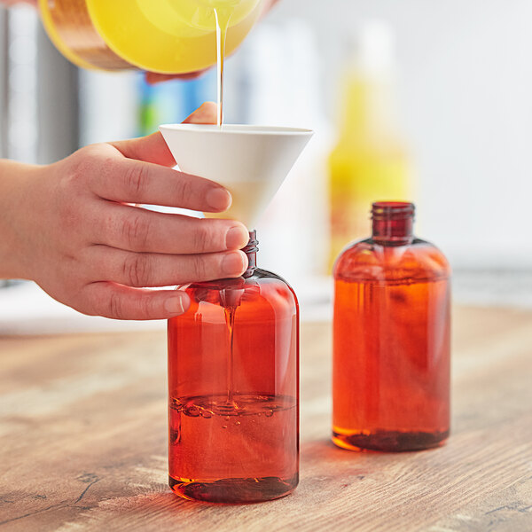 A person pouring liquid into a Boston round amber bottle.