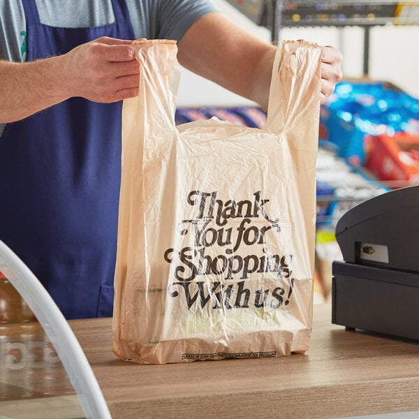 A man holding a beige plastic Source Direct Inc. T-shirt bag with the words "Thank You"