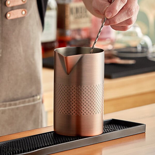 A person using a Barfly copper stirring tin to pour a drink.