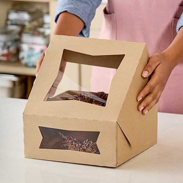 A person holding a Southern Champion bakery box with a window and a frosted cake inside.