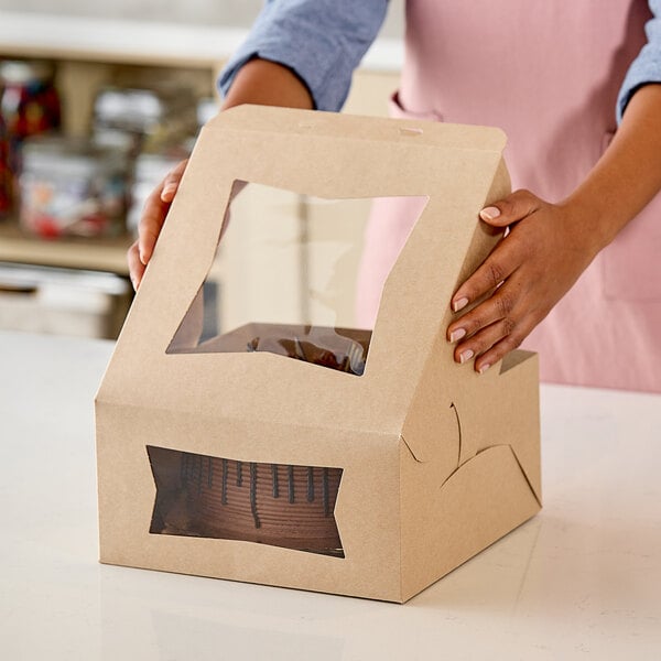 A woman holding a brown Southern Champion cake box with a clear window containing a cake.