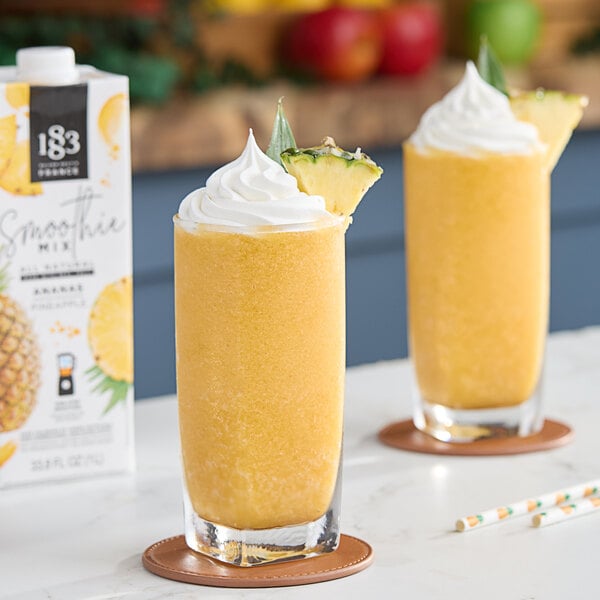 Two glasses of pineapple smoothie with whipped cream and pineapple slices.