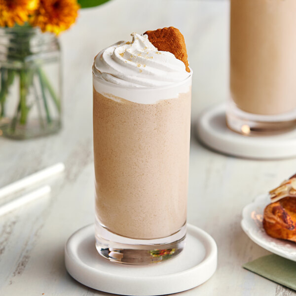 A glass of Cappuccine Supreme Vanilla Latte Frappe with whipped cream and a cookie on the rim.