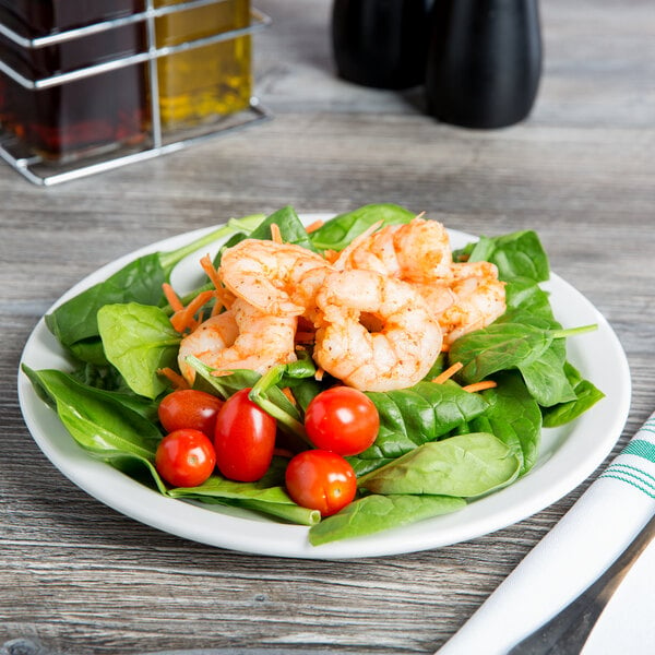 A Libbey round white porcelain plate with shrimp and spinach salad on it.