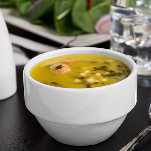 A Libbey Royal Rideau white porcelain bouillon with soup on a black surface.