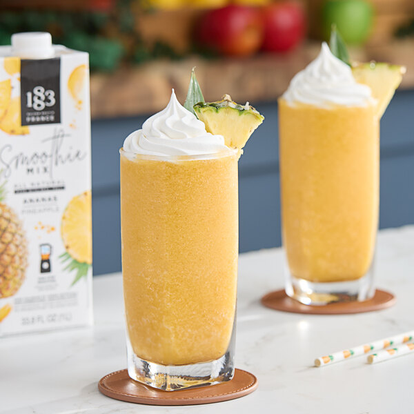 Two glasses of yellow pineapple smoothie with whipped cream and pineapple slices.