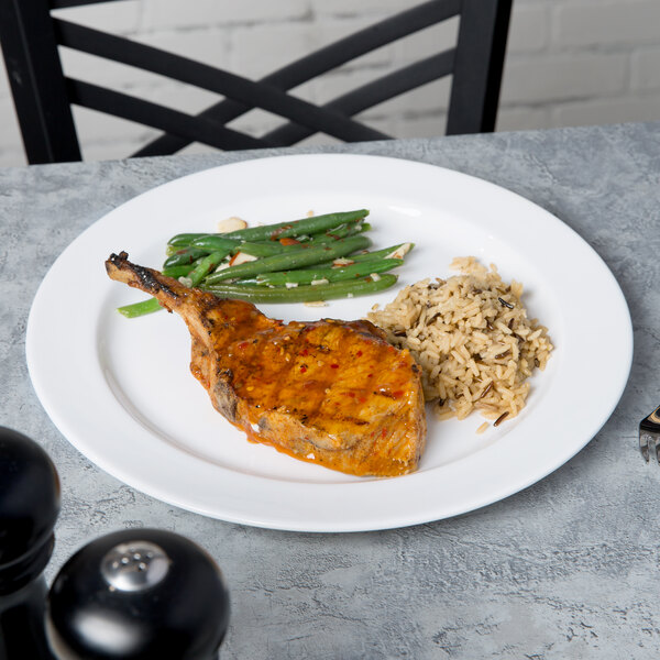 A Libbey Slenda white porcelain plate with a piece of meat and green beans on a table.