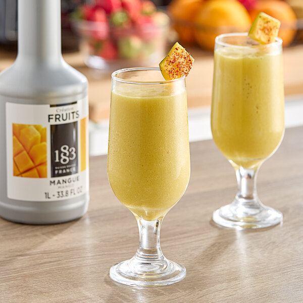 Two glasses of yellow liquid with a slice of mango on top.