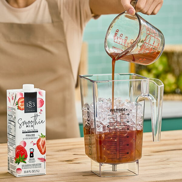 A woman pouring 1883 Maison Routin Strawberry Smoothie Mix into a blender.