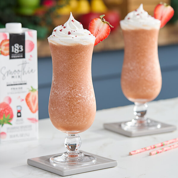 Two glasses of 1883 Maison Routin Strawberry Smoothies with strawberries on top.