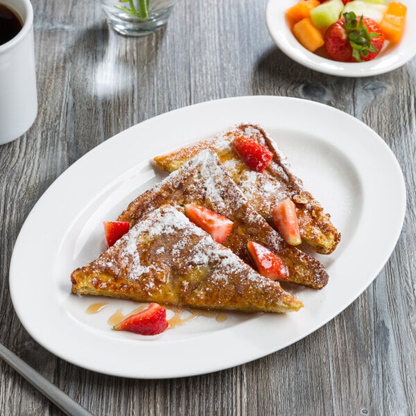 An oval white porcelain platter with a wide rim, shown holding slices of French toast with strawberries and powdered sugar.
