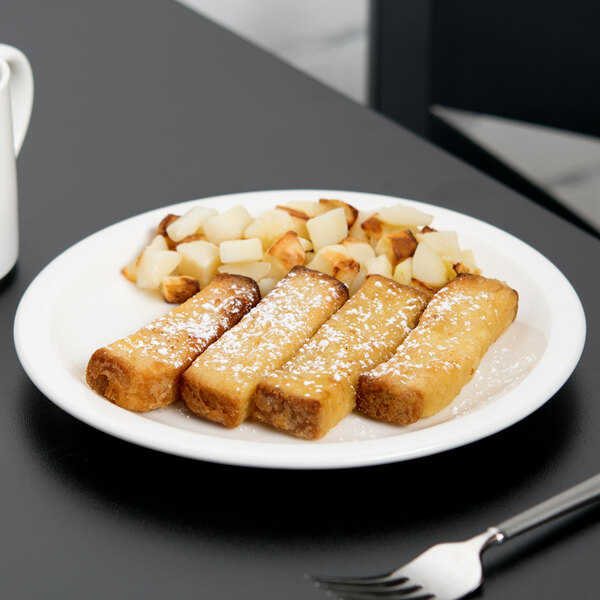 A Libbey Royal Rideau white narrow rim footed porcelain plate with french toast and powdered sugar on a table with a mug of coffee.