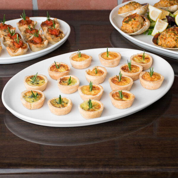 A table with several Libbey Slenda white porcelain trays of food on it.