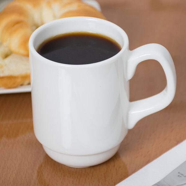 A Libbey white porcelain mug filled with coffee next to a bagel.