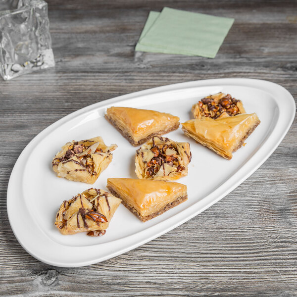 A large, oval white porcelain plate displaying assorted pieces of baklava on a wooden surface.
