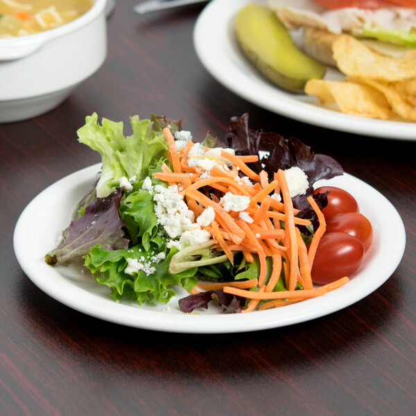 A plate of salad with tomatoes, carrots, and cheese on a Libbey Slenda white porcelain plate.