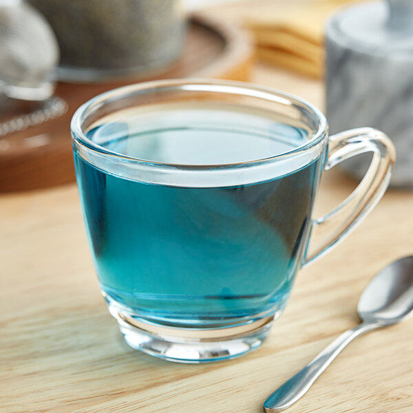 A glass of blue liquid on a table with a spoon.