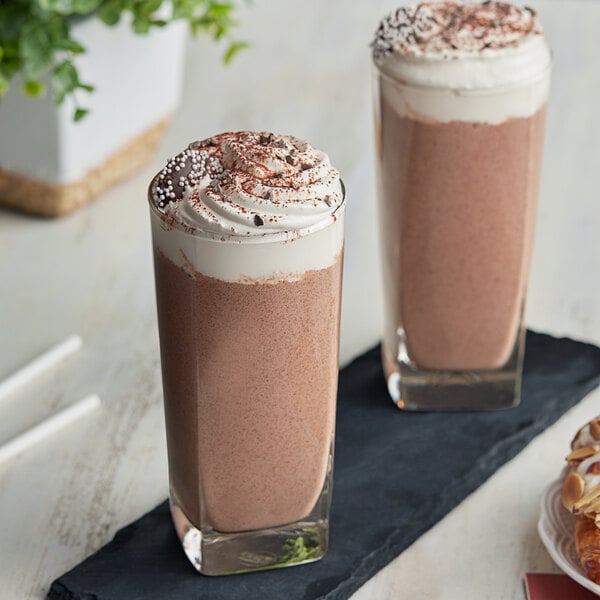 Two glasses of Cappuccine Supreme Chocolate Frappe with whipped cream on top on a table in a brunch cafe.