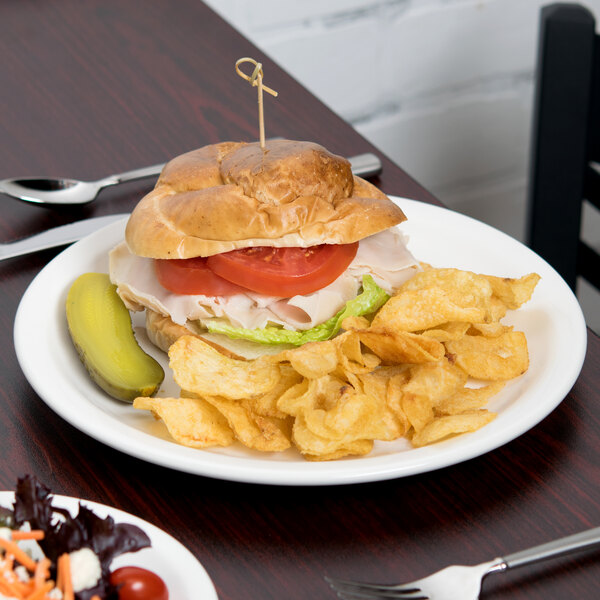 A Libbey white round porcelain plate with a sandwich and chips on a table.