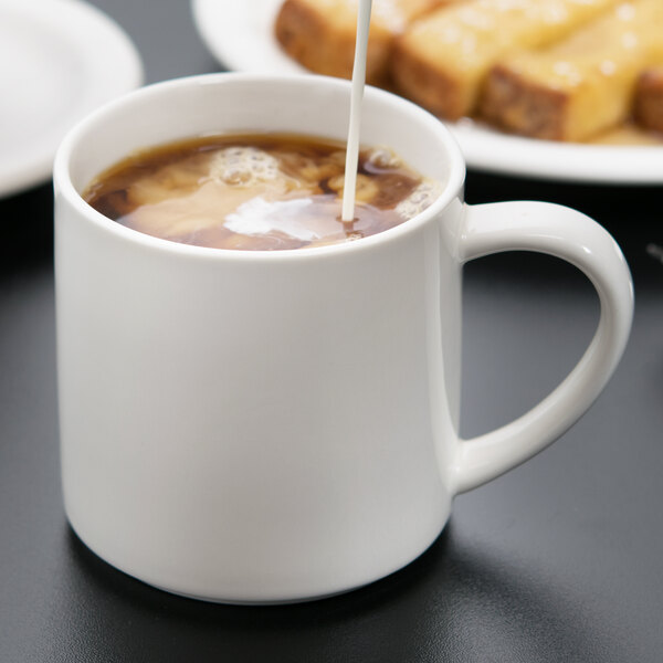 A white porcelain mug filled with coffee, with cream being poured into it.