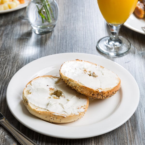 A Libbey Royal Rideau white porcelain plate with a bagel and cream cheese on it next to a glass of orange juice.