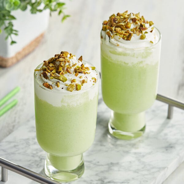 Two glasses of Cappuccine Supreme Pistachio Frappes with whipped cream and pistachio sprinkles.