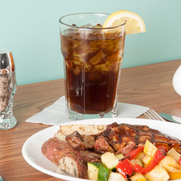 A plate of food and a Libbey Gibraltar beverage glass filled with ice on a table.