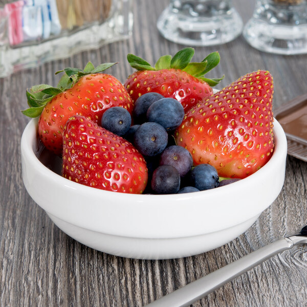 A Libbey Slenda white porcelain fruit bowl filled with strawberries and blueberries on a table.