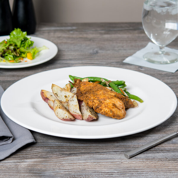 A Libbey Slenda white wide rim footed porcelain plate with food on a table.