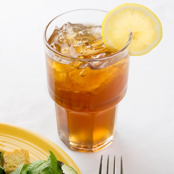 A Libbey stackable beverage glass of ice tea with a lemon slice on top of it.