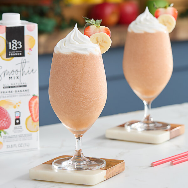 Two glasses of 1883 Maison Routin strawberry banana smoothie with strawberries and bananas.