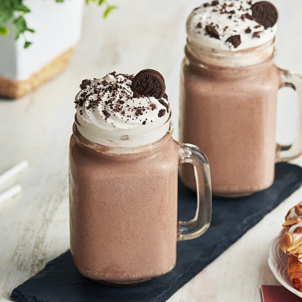 Two glass mugs filled with Cappuccine Cookies & Cream frappes topped with whipped cream and cookies.