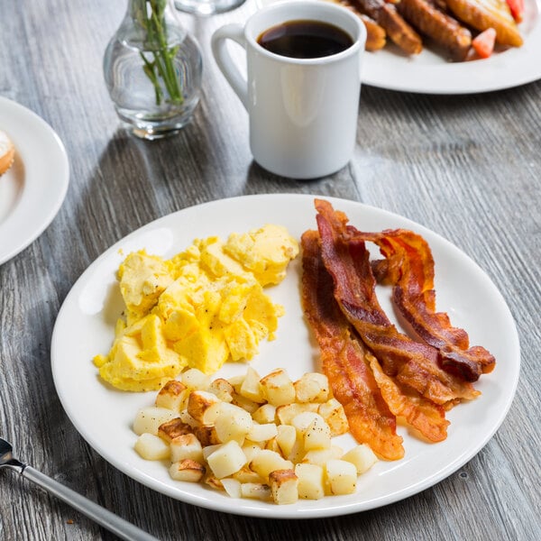 A Libbey Royal Rideau coupe plate with eggs, bacon, and potatoes on a table.