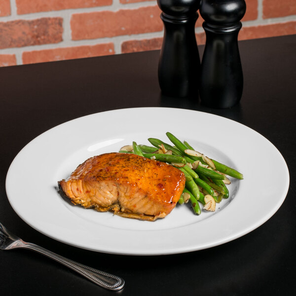 A Libbey white porcelain plate with salmon and green beans on a table with a fork.