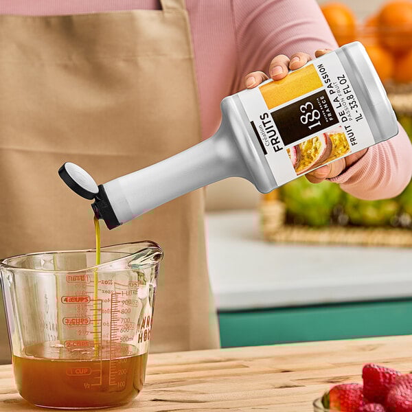 A woman pouring 1883 Maison Routin Passion Fruit puree from a bottle into a measuring cup.