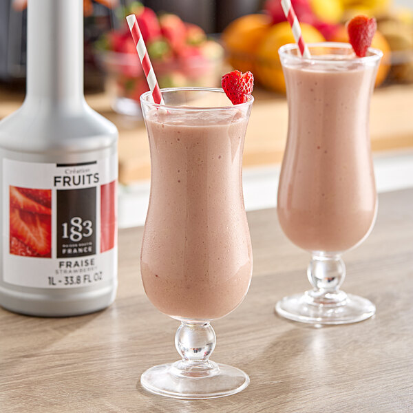 Two glasses of strawberry smoothie with red and white striped straws and a bottle of 1883 Maison Routin Strawberry Puree.
