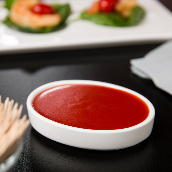 A Libbey Royal Rideau White stacking porcelain oval bowl with red sauce and shrimp on a table.