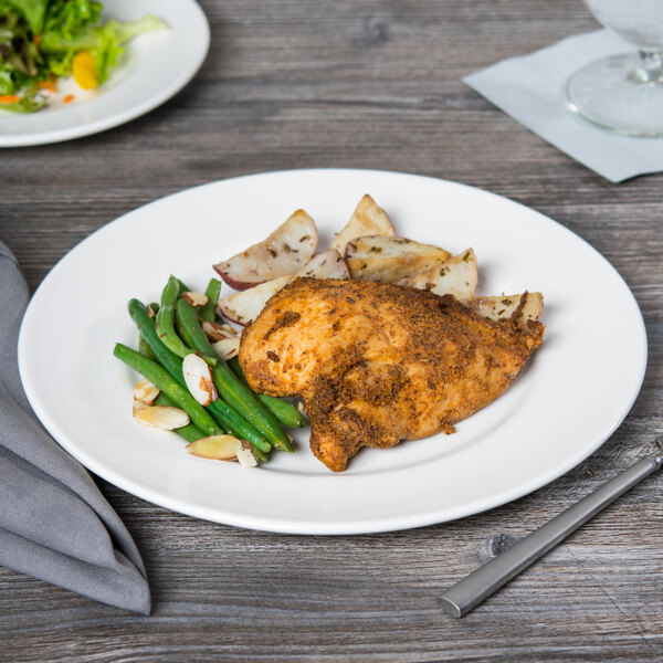 A Libbey white porcelain plate with food on a table with a fork and knife.