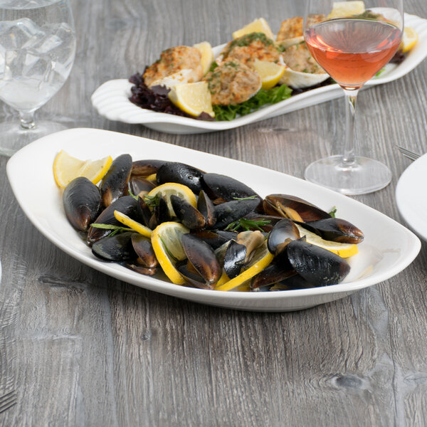 A Libbey white porcelain platter with mussels and lemons on a table.