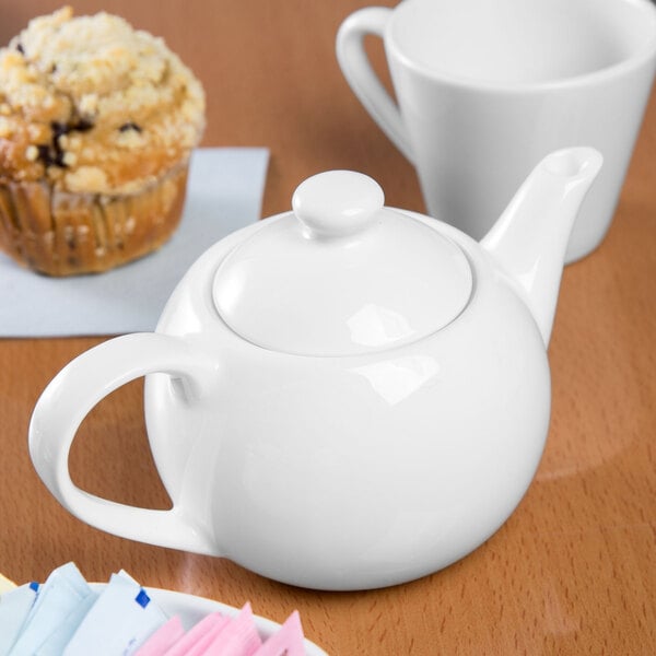 A white Libbey Slenda porcelain tea pot on a table with a cup of tea.