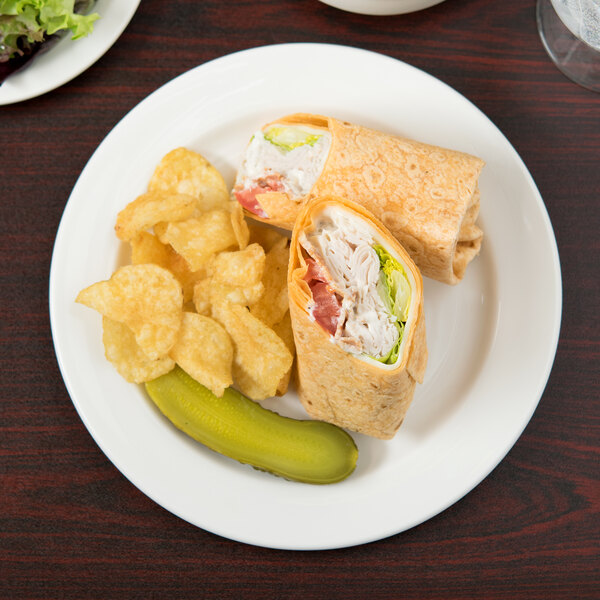 A Libbey round white porcelain plate with a sandwich and pickles on it.