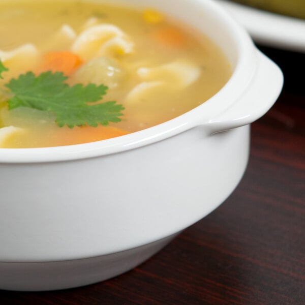 A white Libbey Slenda porcelain soup cup with two handles filled with soup and vegetables.