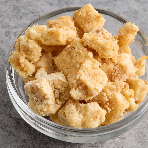 A bowl of Ice Cream Factory Cheesecake Bites on a table with graham cracker crumbs and cookie pieces.