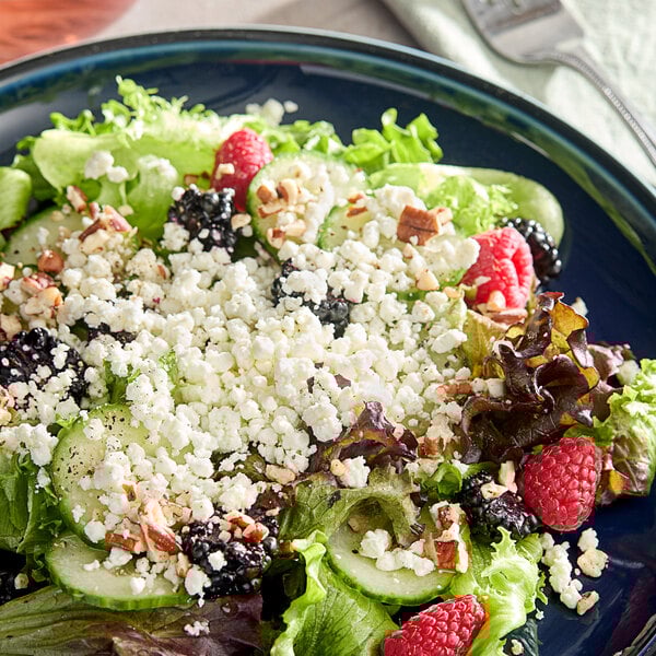 A salad with berries and Celebrity Goat crumbled goat cheese on a plate.