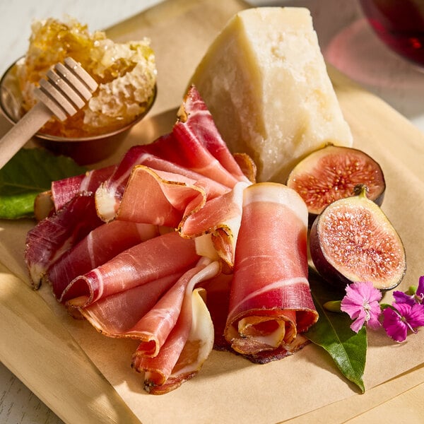 A platter featuring slices of dry-cured smoked speck, a wedge of cheese, figs, honeycomb, and garnishes.