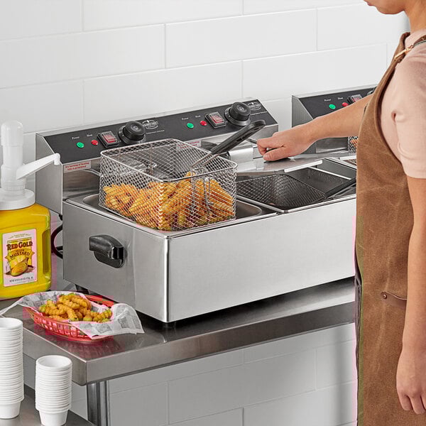 A woman using a MainStreet Equipment dual tank electric countertop fryer to cook fries in a commercial kitchen.