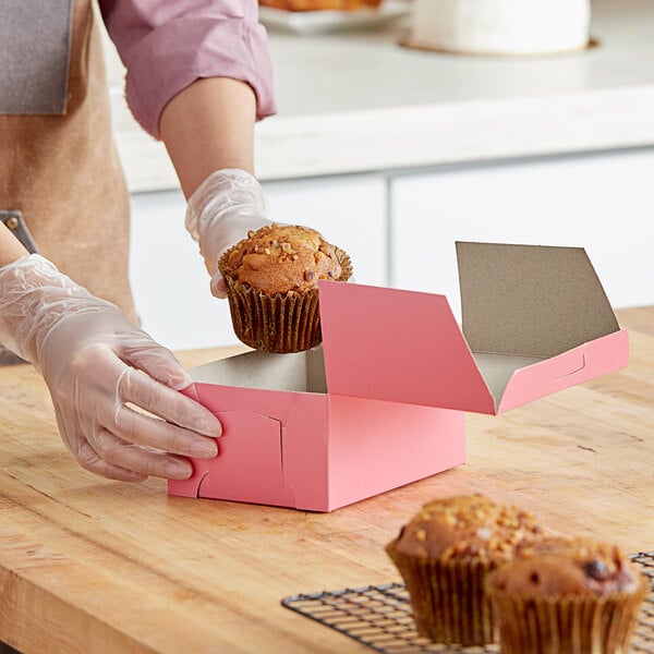 A person holding a muffin and putting it into a pink Southern Champion bakery box.