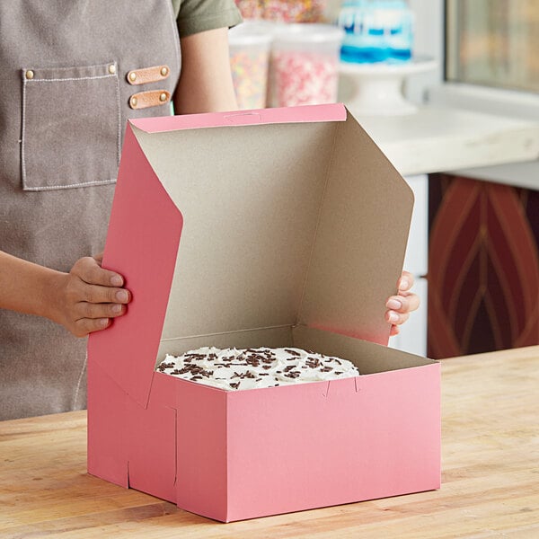 A woman holding a pink Southern Champion cake box with a white cake inside.