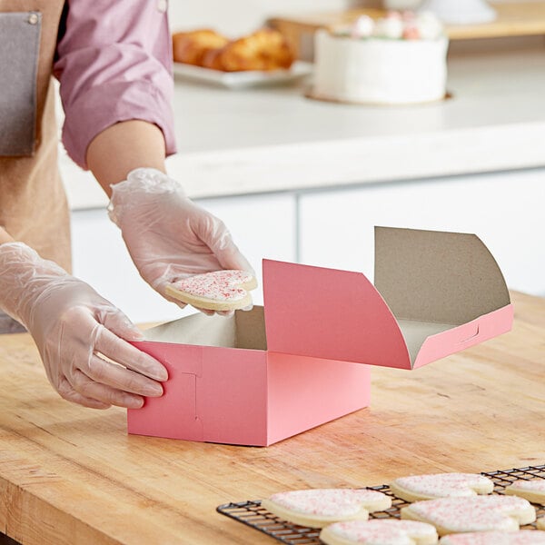 A person wearing gloves puts a heart-shaped cookie in a pink Southern Champion bakery box.