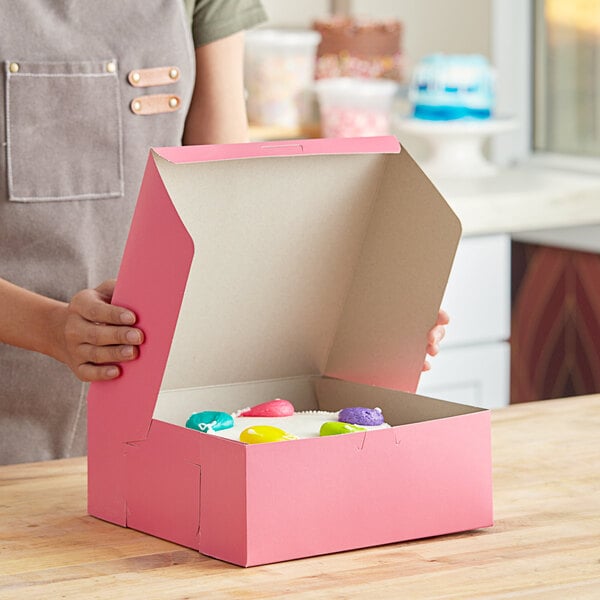 A woman holding a pink Southern Champion bakery box with white frosting on a cake inside.